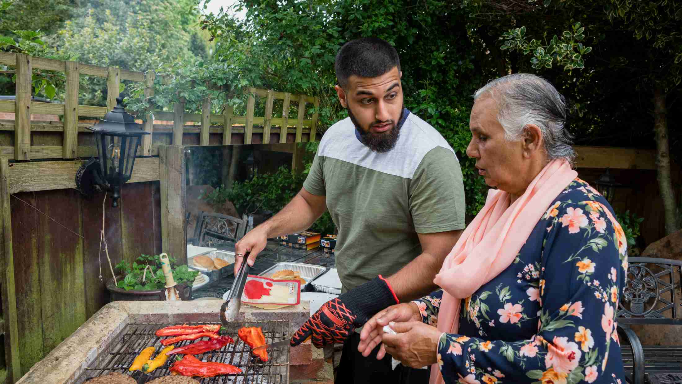 Grandson and grandmother in a garden cooking on a BBQ together