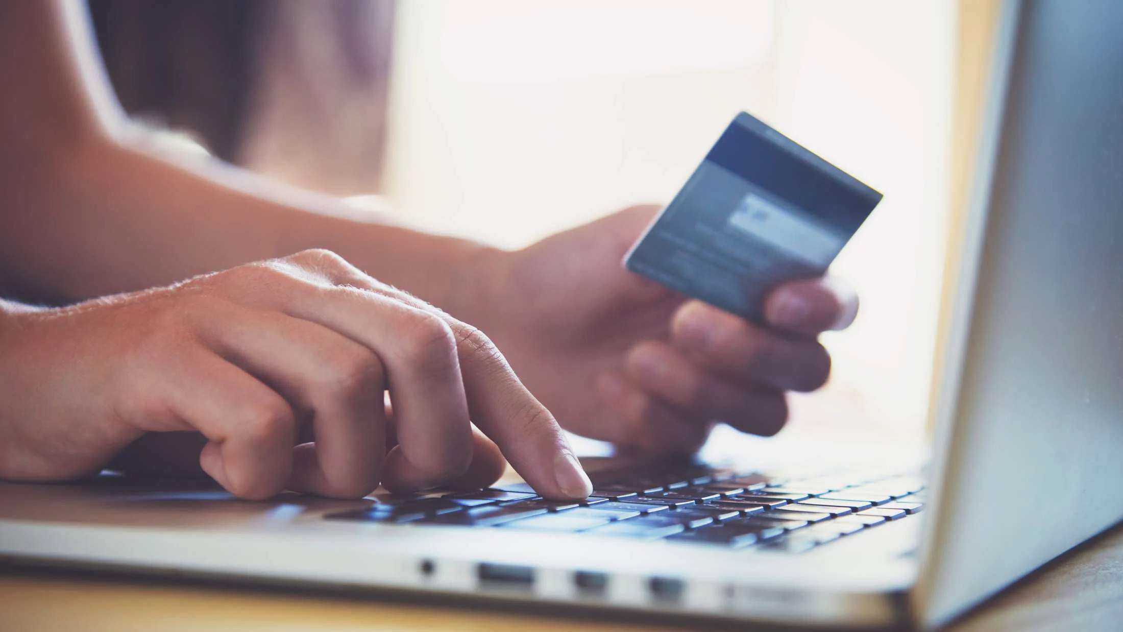 Hand holding credit card while using laptop