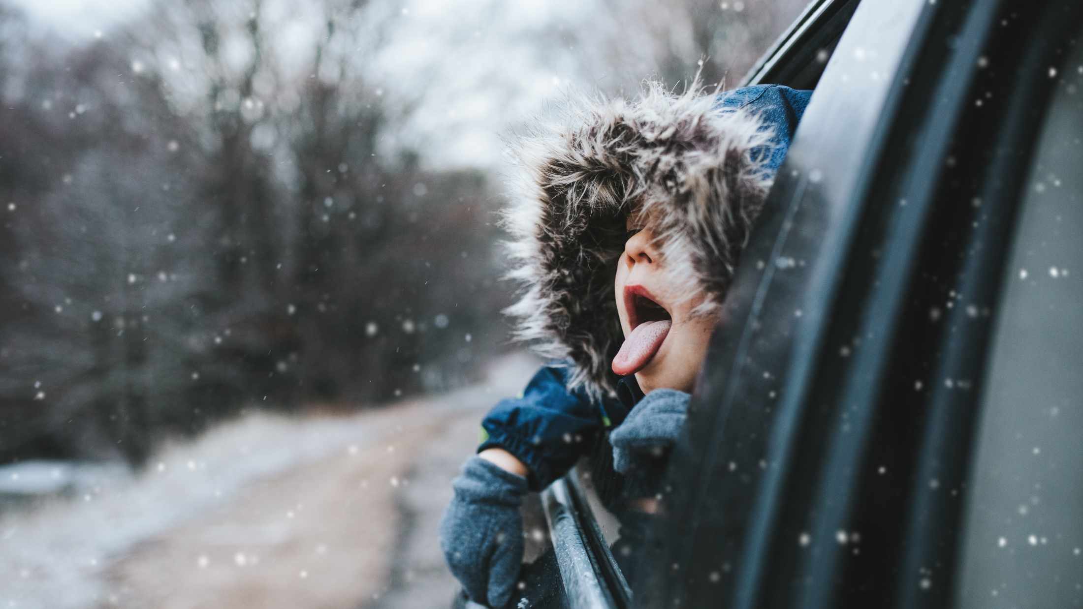 Little boy leaning out of a car window wearing a parka jacket