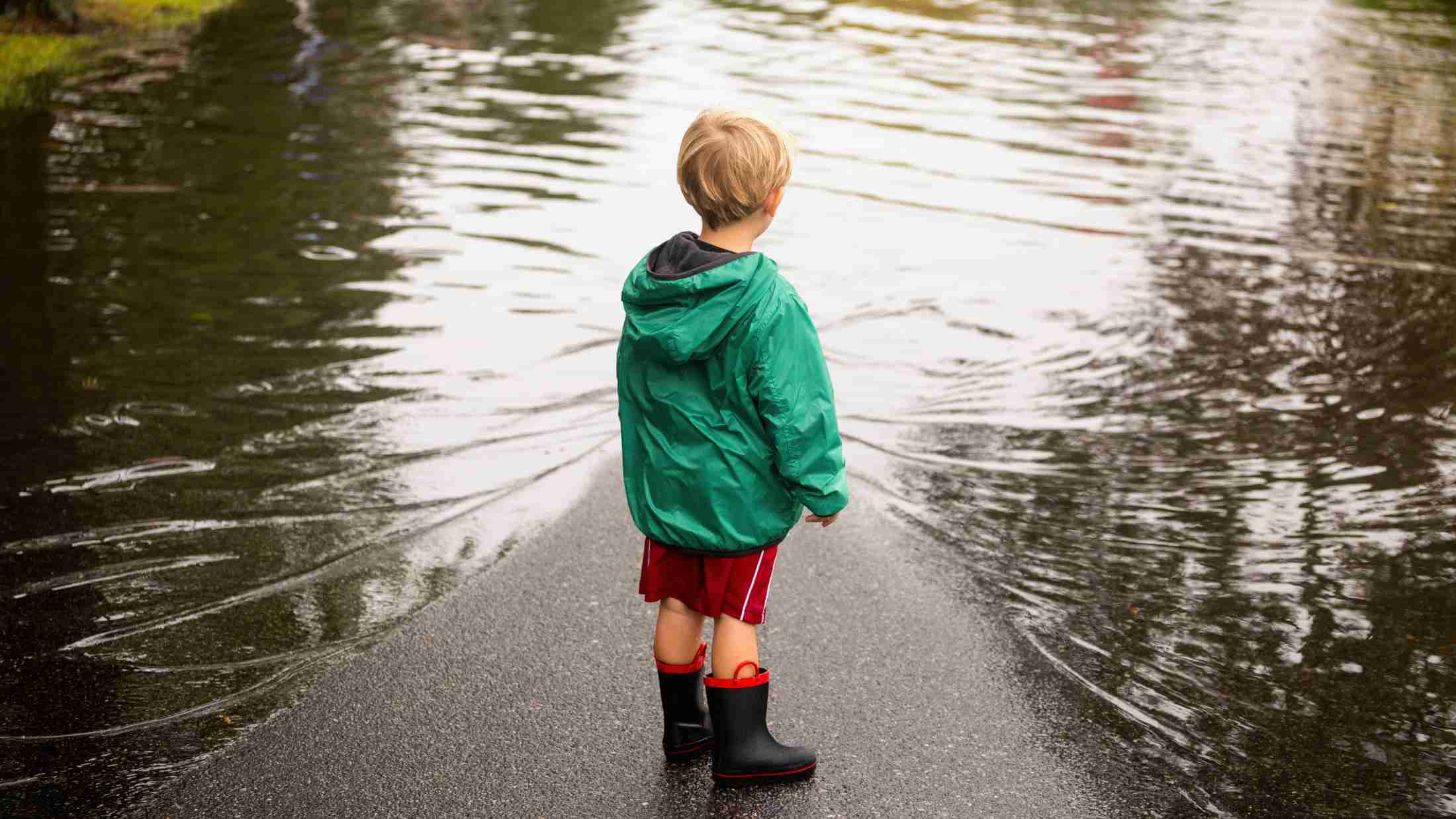 Young boy wearing wellies and an anorak as he stands near flood puddles